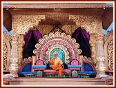 Swamishri seated on a colorful giant stage, serenely chanting the holy name of Swaminarayan