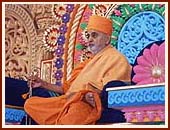 Swamishri seated on a colorful giant stage, serenely chanting the holy name of Swaminarayan