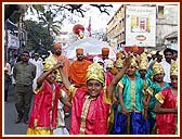 Saints pull a float with Lord Swaminarayan's murti, while children dance in front