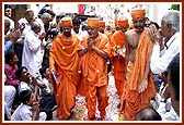 Swamishri is given a glorious and jubiliant welcome as he walks through Ambli Vali Pol*. The devotees joyously shower flowers and chorus thunderous 'Jays' in honor of Swamishri. * A cluster of adjoining homes with a narrow gully and a single entrance door