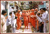Swamishri is given a glorious and jubiliant welcome as he walks through Ambli Vali Pol*. The devotees joyously shower flowers and chorus thunderous 'Jays' in honor of Swamishri. * A cluster of adjoining homes with a narrow gully and a single entrance door