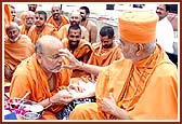 Swamishri ties nada-chhadi and applies chandlo to  P. Ishwarcharan Swami
