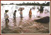 Sadhus and volunteers cross flooded areas by boat and on foot to deliver relief supplies to flood victims