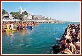 Swamishri on a raft in the river Ghela. Sadhus and devotees fill every vantage point to enjoy this divine darshan 