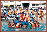 Swamishri on a raft in the river Ghela. Sadhus and devotees fill every vantage point to enjoy this divine darshan 