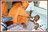 Swamishri is apprised of Shrujan Singh's condition, the NSG commando injured during Operation Thundernight, by the doctors and blesses him and prays for his recovery. Swamishri gently blesses him with the touch of his hand and showers sacred rose petals