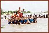 Sadhus pull Swamishri's decorated raft back to shore.