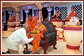Swamishri holds a walking stick, mala and bouquet for an aged devotee as he stands up