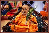 Swamishri holds a walking stick, mala and bouquet for an aged devotee as he stands up