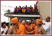 Kishores seated on the roof enthusiatically receive Swamishri