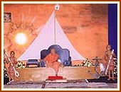 Swamishri in a boat-like seat with an ocean backdrop in the evening assembly, 7 Oct 99