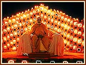 Swamishri during the welcome assembly, with a backdrop of bricks and lamps illuminating the stage. 2 Dec 99