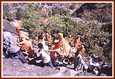 Swamishri being carried through narrow and steep pathways towards the caves