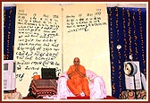 Swamishri after completing his morning puja. Backdrop of a magnified page of diary in Swamishri's on words about the day of his appontment as president