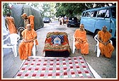 Swamishri sits on an ordinary chair with Thakorji placed on a decorated sofa on the road outside his residence