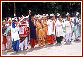 Kishores and youths dressed in traditional clothes jubilantly welcome Swamishri and the entourage of sadhus to the mandir
