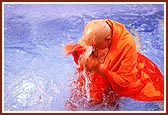 Swamishri takes a dip in a pool and blesses the devotees by sprinkling water