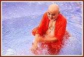 Swamishri takes a dip in a pool and blesses the devotees by sprinkling water