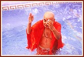 Swamishri takes a dip in a pool and blesses the devotees by sprinkling water