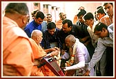 &nbsp;&nbsp;Swamishri blesses and soothes an accident victim and presents a sanctified flower of Thakorji