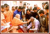 &nbsp;&nbsp;Swamishri blesses and soothes an accident victim and presents a sanctified flower of Thakorji