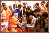 &nbsp;&nbsp;Swamishri blesses and soothes an accident victim and presents a sanctified flower of Thakorji