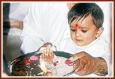 A child first curiously looks on and then joins his father in performing the patotsav arti