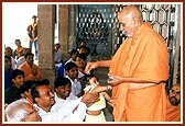 Swamishri blesses the devotees and their children by showering rice grains