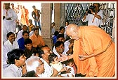 Swamishri blesses the devotees and their children by showering rice grains