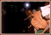 Swamishri and senior sadhus place the first lighted divas into the holy river Ghela