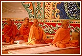 Senior sadhus seated on stage engrossed in darshan of Swamishri's morning puja