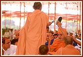   Swamishri holds aloft a device released by Swaminarayan Aksharpith that plays Swaminarayan dhun while the sadhu in foreground holds a microphone