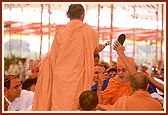 &nbsp;&nbsp;Swamishri holds aloft a device released by Swaminarayan Aksharpith that plays Swaminarayan dhun while the sadhu in foreground holds a microphone