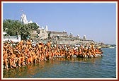 Sadhus seated on the banks of river Ghela engrossed in darshan of Swamishri while he bathes Shri Harikrishna Maharaj
