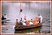Swamishri, senior sadhus and trustees arrive by boat for the murti pratishtha ceremony of Shri Sarveshwar Mahadev in the lake called Sursagar. In the background is the famous Nyaya Mandir