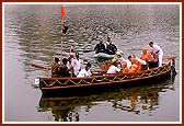 Swamishri, senior sadhus and trustees arrive by boat for the murti pratishtha ceremony of Shri Sarveshwar Mahadev in the lake called Sursagar. In the background is the famous Nyaya Mandir
