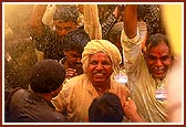 Devotees ecstatically fold their hands to be blessed with the shower of holy, colored water