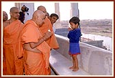A little boy folds his hands in respect and Swamishri blesses him with a sanctified flower