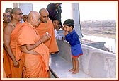 A little boy folds his hands in respect and Swamishri blesses him with a sanctified flower