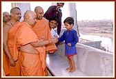 A little boy folds his hands in respect and Swamishri blesses him with a sanctified flower