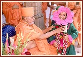 Swamishri places the sanctified garland around the balak's neck and pleases him 