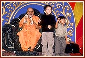 On Children's Day assembly, little children dance to the singing of a bhajan during a kirtan concert. Swamishri participates by playing the kartal