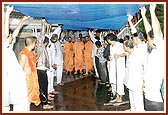Volunteers hold a canopy for Swamishri during the rain