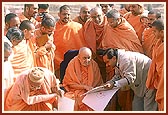 Swamishri observes the plans and discusses about the complex. In the background are sections of the parikrama