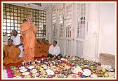 Swamishri engaged in Thakorji's darshan, with the annakut items arranged in the foreground