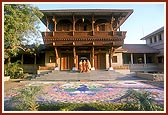 Swamishri on his way for Thakorji's darshan from the recently built haveli. In the foreground is a beautiful rangoli 