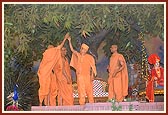 Swamishri arrives on stage for a special assembly for volunteers. The stage backdrop, 'Yagnapurush Fulvadi', was meticulously prepared by sadhus. Swamishri feels the decoration.