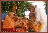 Swamishri sprays the sanctified colored water on a leading devotee