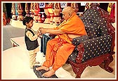 Swamishri gives a small garland to a child who wandered onto the stage