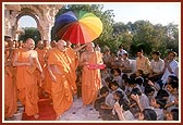 Due to weakness Swamishri places his hand on Pujya Ghanshyamcharan Swami's head while he showers rose petals on his behalf upon students prior to their exams